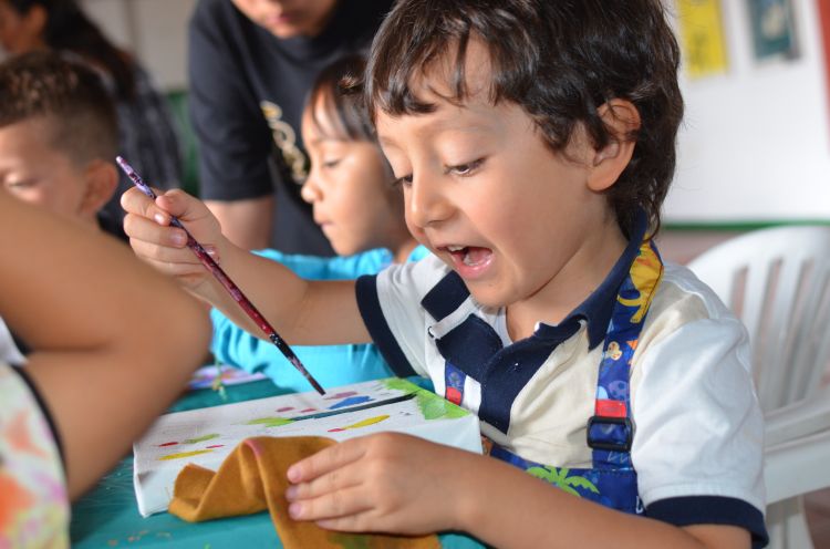 A young boy dipping a paint brush into paint.