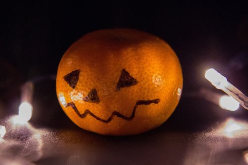 A mandarin orange with a jack-o-lantern face drawn on it.