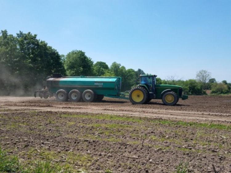 A tractor pulls a container spreading manure in a field.