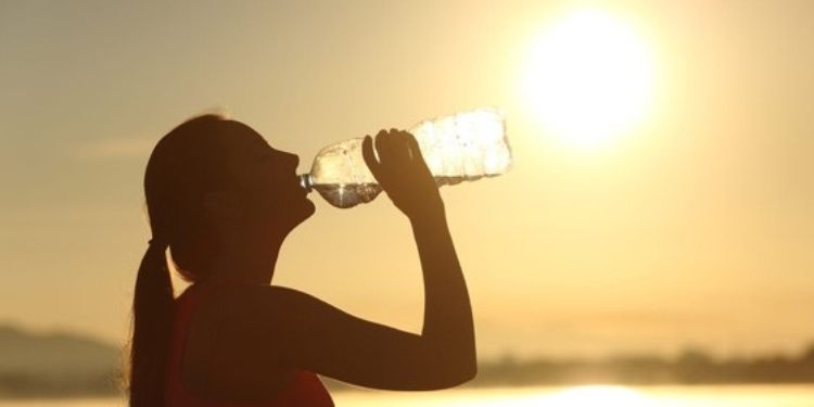 girl with pony tail drinking water at sunset