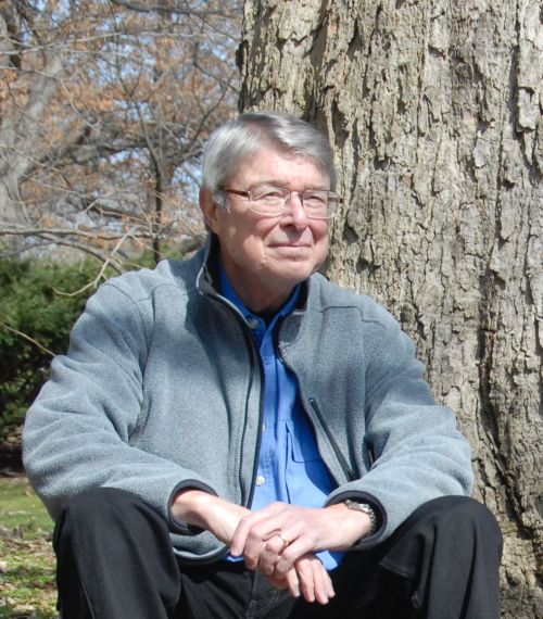 Emeritus faculty member Donald Dickmann in a gray sweater sitting against a tree outdoors.