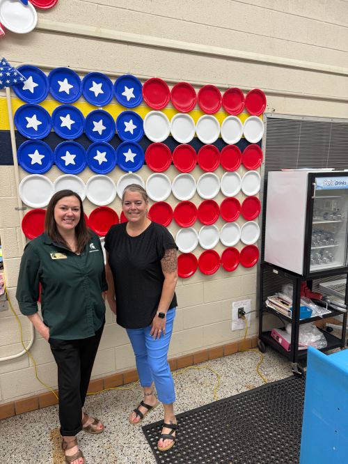 Julia Simon and Bendle Public Schools Food Service Director Dawn Pully standing in front of an American flag made out of plates.