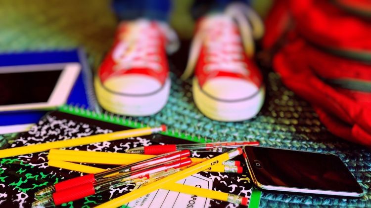 A pair of youth sneakers with notebooks, pencils, pens and other back to school supplies.