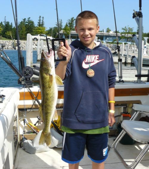 Young boy holds up walleye while standing on a boat.