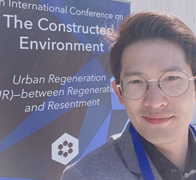 Image of Juntae Jake Son in front of The Constructed Environment Conference sign.