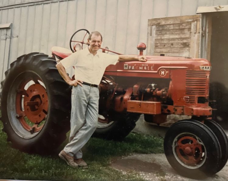 Image of Harold (Hal) Bernthal (’50, Chemistry) standing in front of a red tractor.