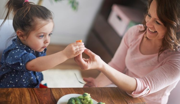 A caregiver helping a young girl try fresh produce.