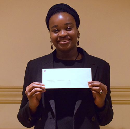 Image of Najma holding a white envelope containing her scholarship.