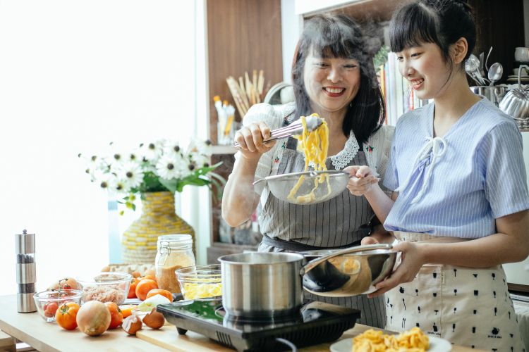 A mother and teen daughter cooking in a kitchen together.