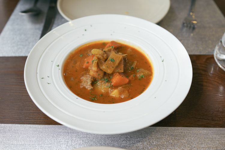 Brown soup in white bowl with vegetables.