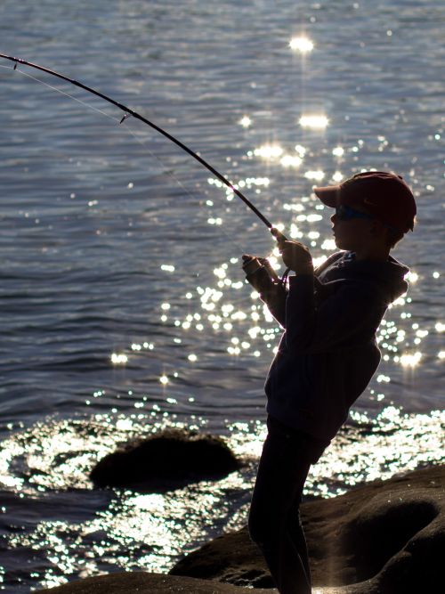 Young boy fishing along coast.