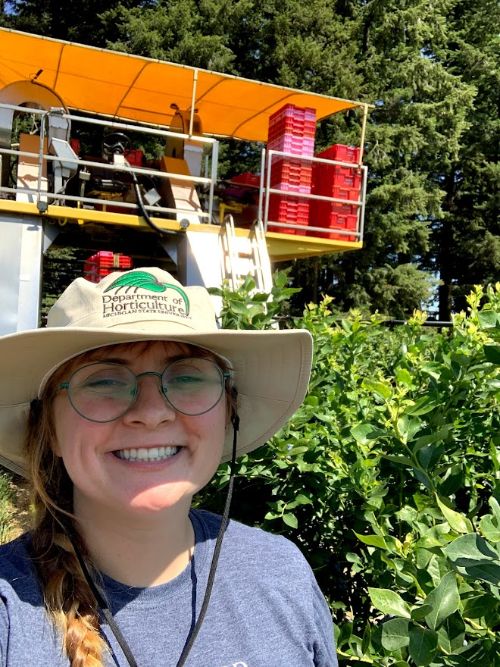 Cheyenne Sloan smiling in front of a blueberry research plot.