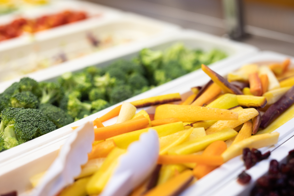 Multicolored carrot sticks and green broccoli florets in a school cafeteria salad bar.