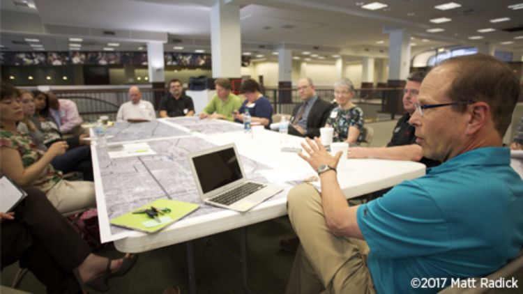 Image of Bill Lennertz presenting to a group of stakeholders seated at a table during a charrette.