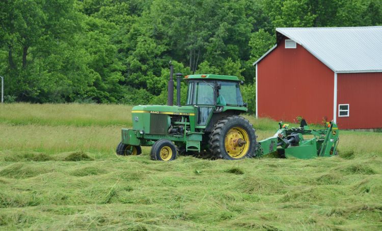green tractor cutting green hay in front of a red barn