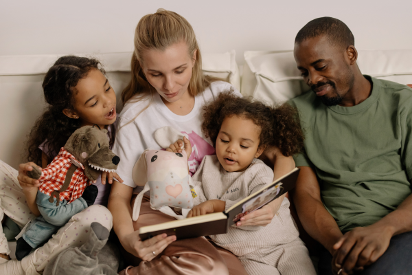 Two adults reading a book to two young children.