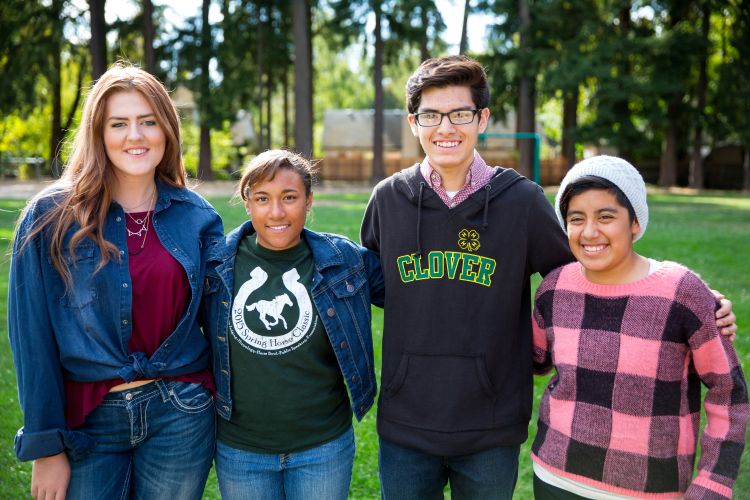 Four diverse 4-H youth standing in a park with trees in the background.