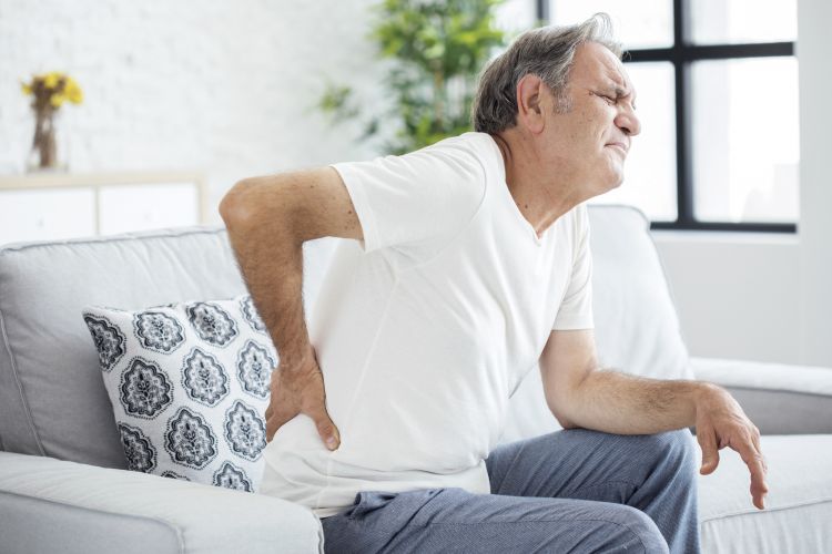 An older male-presenting person clutching their back and wincing in pain.