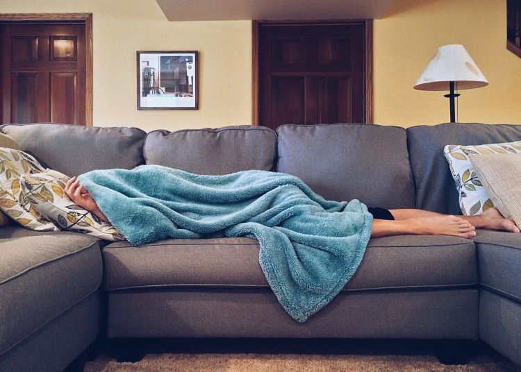A woman laying on a couch covered up in a blanket recovering from sickness.