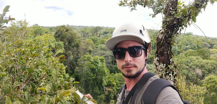 Leonardo Ziccardi above the canopy in a tree holding the MultispeQ device, with the vast Amazon rainforest stretching into the background.