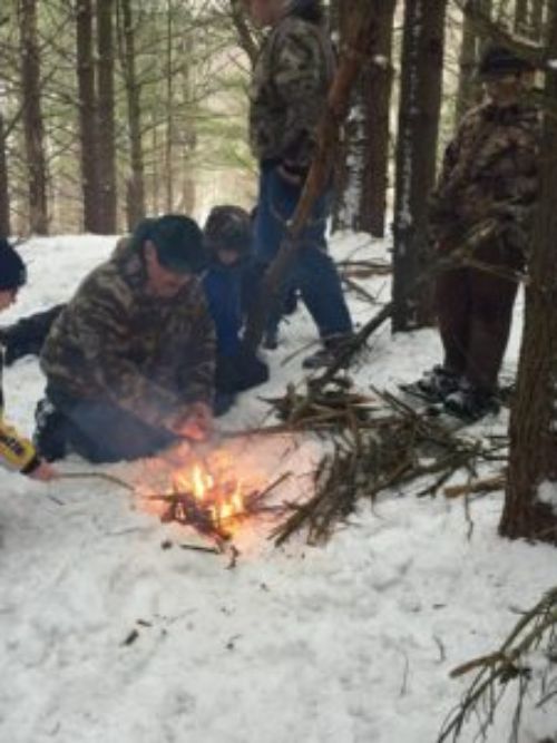 Man teaching children how to start a fire in the snow.