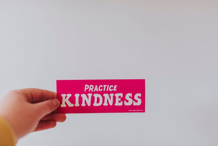 Hand holding a sign saying practice kindness