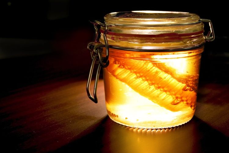 A glass jar filled with honey against a dark background.