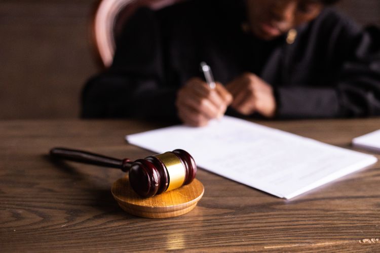 Judge signing a sheet of paper at a desk with a gavel resting on it.