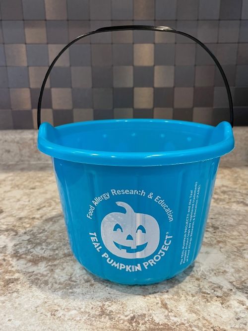 A teal colored Halloween treat pail with a pumpkin on it.