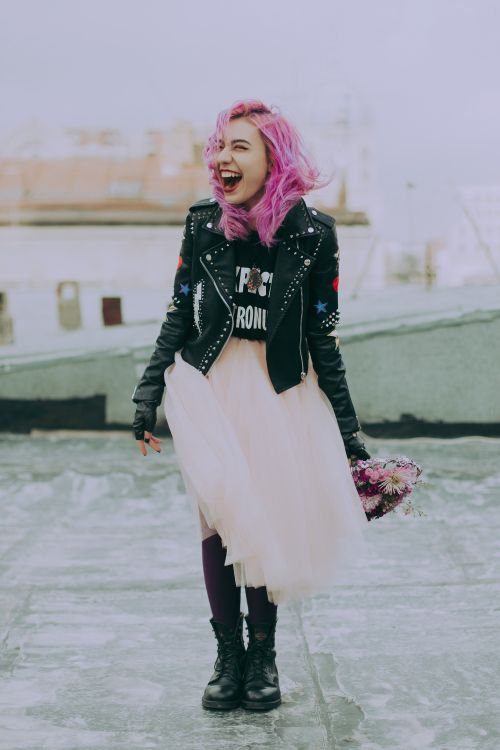 A young woman with pink hair laughing outside.