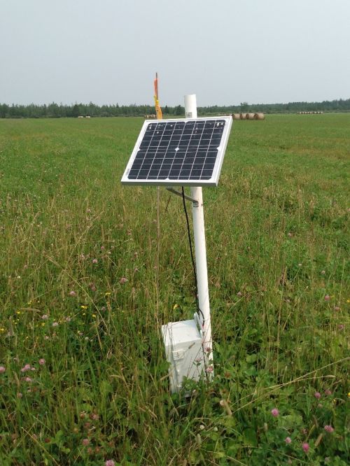 A solar panel attached to a white pole in the ground in the middle of a field.