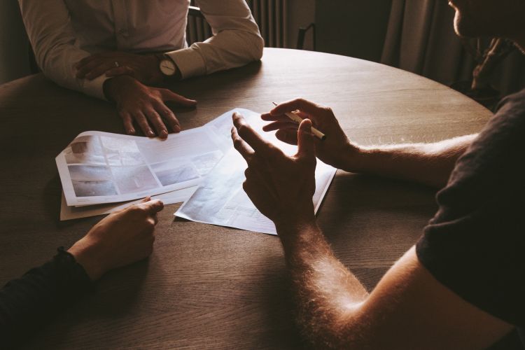 Three men at table with paperwork in front of them.