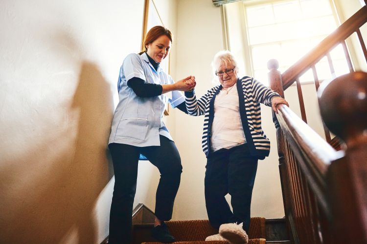 A caregiver helping an elderly woman down the stairs.