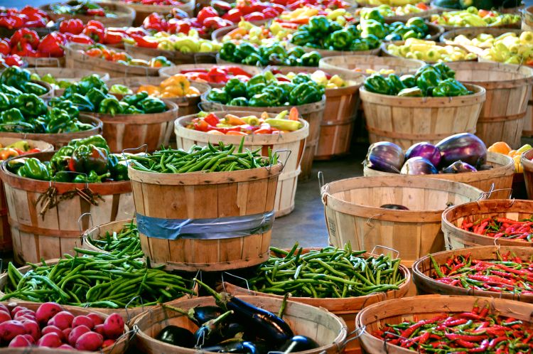 A couple dozen or so wooden baskets filled with an array of vegetable crops at a farmers market.
