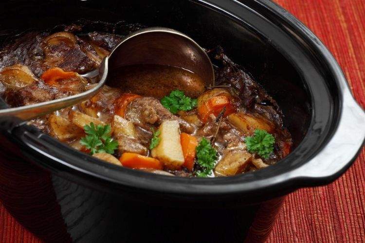 An open slow cooker filled with beef stew, with a ladle resting in it.