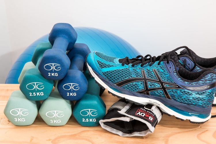 Various exercise equipment on a table, such as a running shoe and a pyramid of dumbbells.