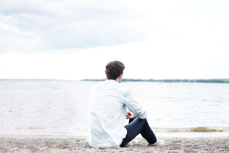 Man sitting alone on a pebbled beach