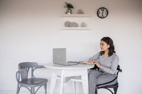 Woman sitting with laptop on table taking notes.