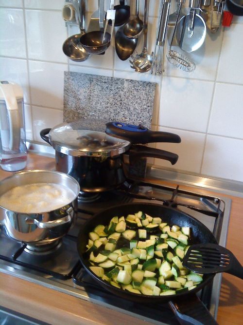Stove with pressure cooker, zucchini, and boiling corn in pot.