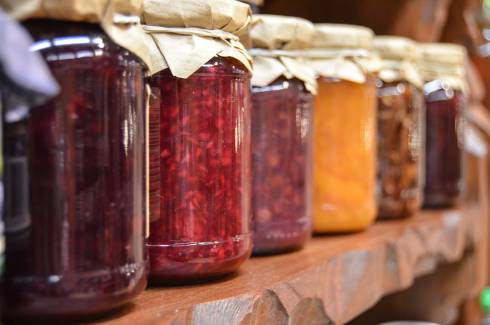Jam and Jelly jars lined up on a wooden shelf.