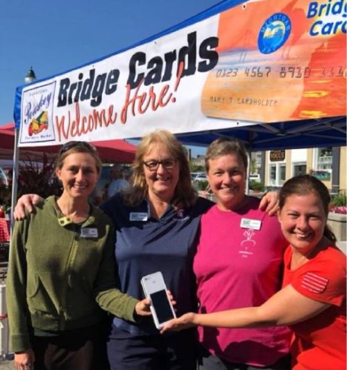 Four women stand under a Bridge Card sign.