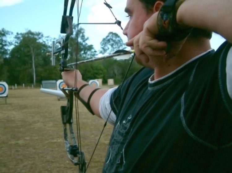 A man pulling back a hunting bow, aiming at a bullseye target.
