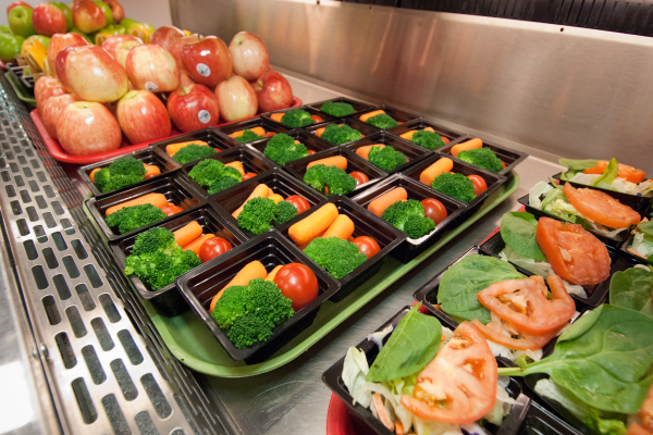 Cafeteria trays full of fresh fruits and vegetables.