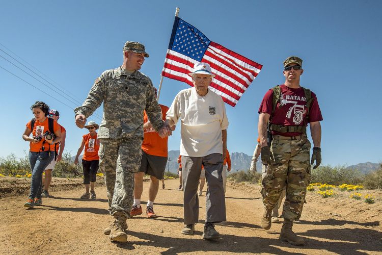 A group of soldiers walking with an American flag.