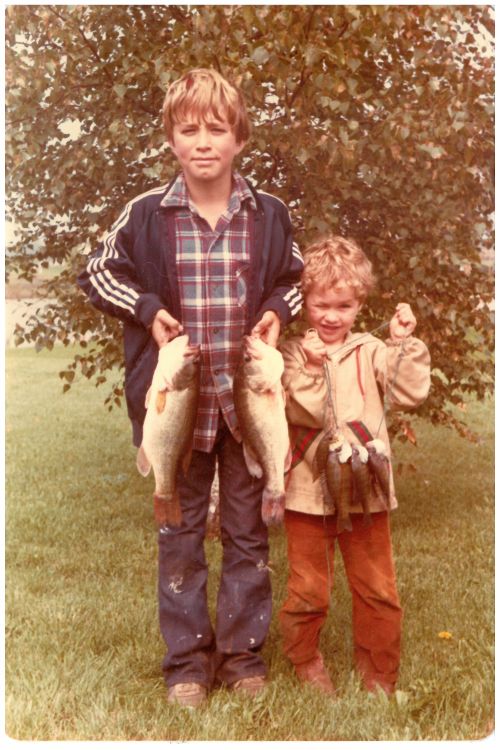 Older photo showing two young boys each holding several fish they have caught standing in front of a tree.
