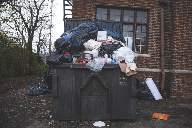 Overflowing trash dumpster in front of a brick building.