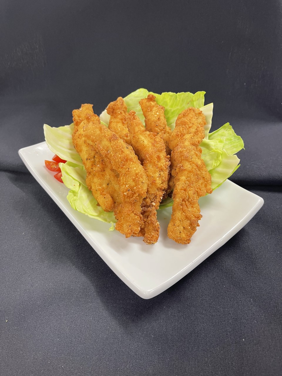Three chicken tenders coated and fried in bean flour on lettuce and placed on rectangular plate.