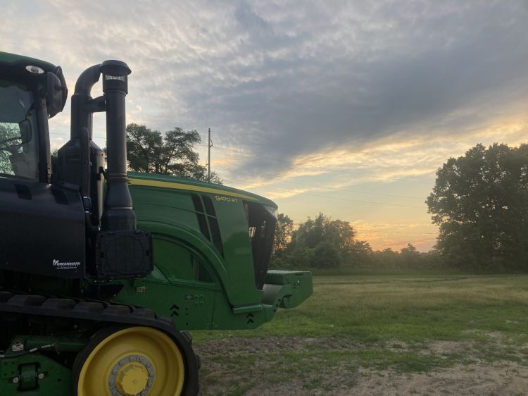 A tractor in a field with the sun setting in the background.