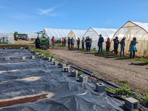 About 20 farmers standing near hoophouses and farm fields.