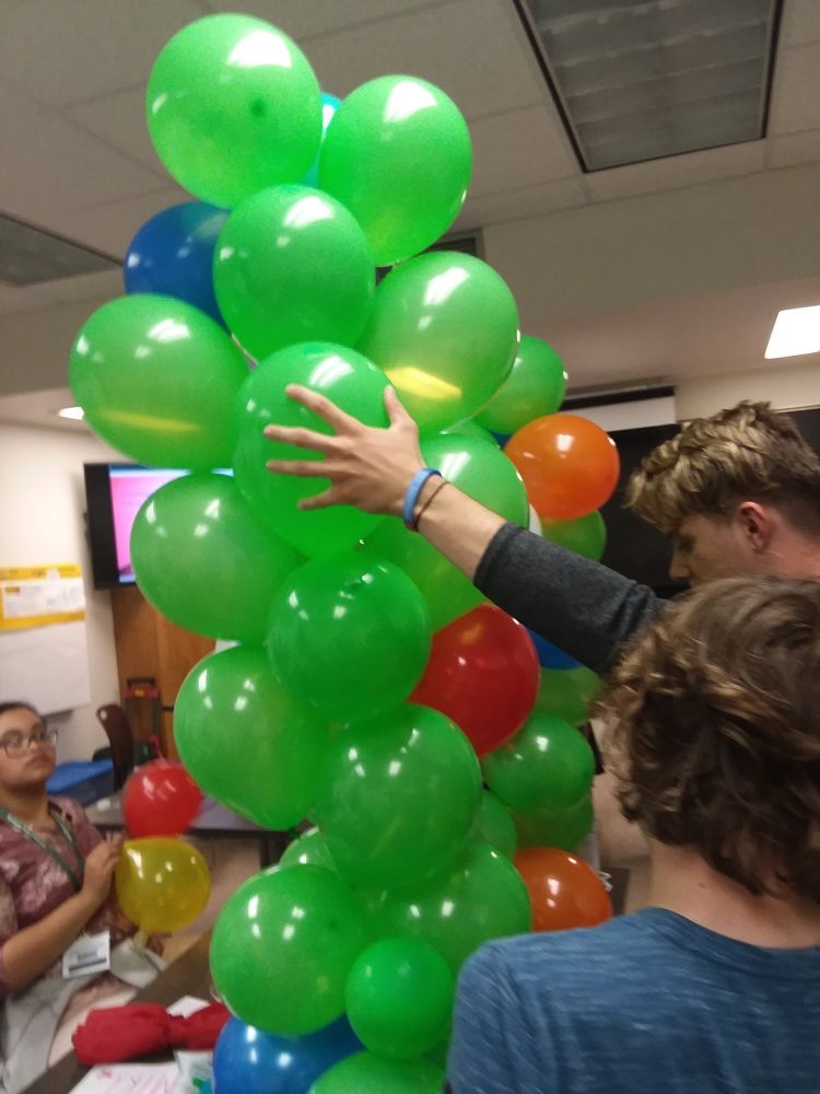 Youth standing next to a tower of balloons.